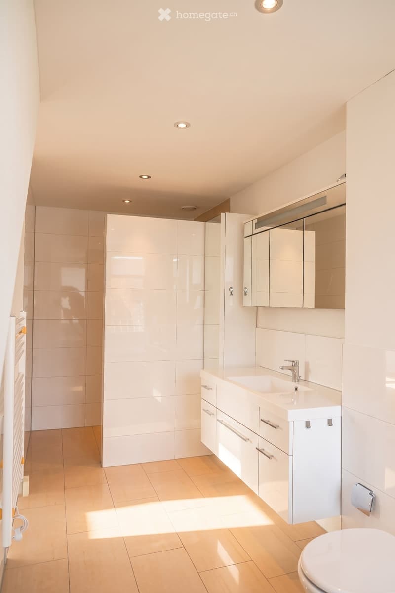 Modern bathroom with white tiles, a sink, a mirror, and a toilet. The room features built-in cabinets and recessed lighting.