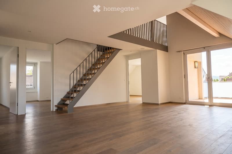 Bright, open-plan space with wooden flooring, modern staircase, large windows, and a balcony overlooking the area.