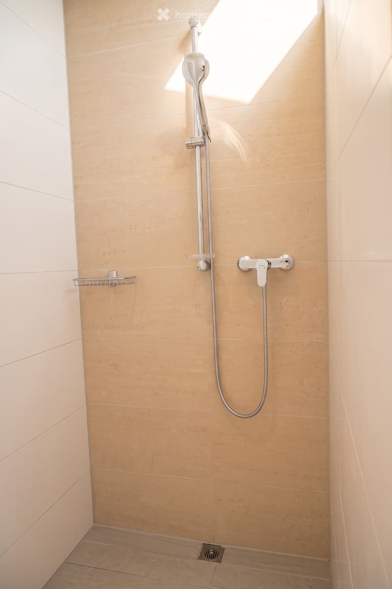 Modern bathroom shower area with beige tiles, a handheld showerhead, a fixed showerhead, a chrome faucet, and a small shower rack.