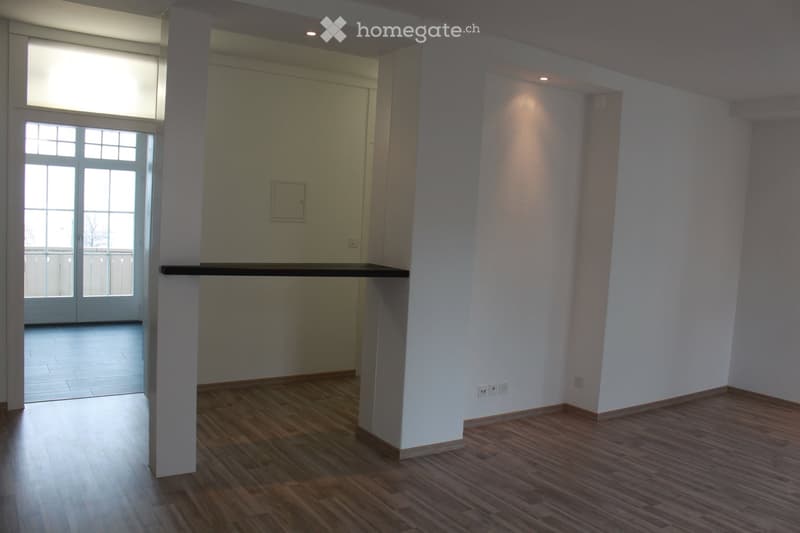 Empty room with wooden flooring, white walls, and a large window with glass doors leading to a balcony.