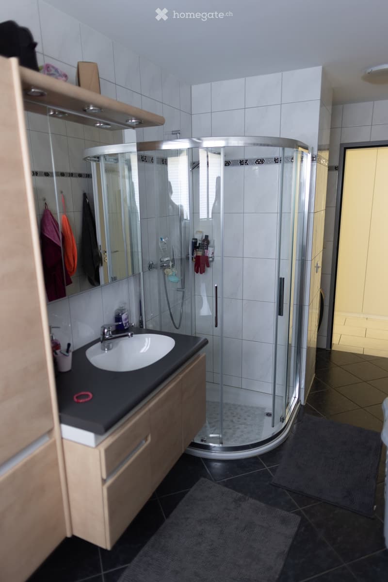 Modern bathroom with a white tiled shower stall, a black countertop sink, and wooden cabinetry. Includes a mirror, towels, and various bathroom accessories.