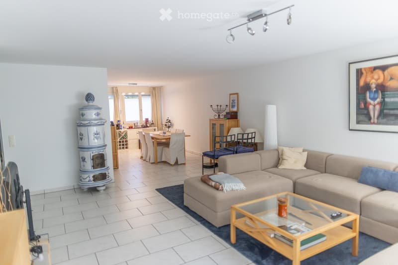 Modern living room with a beige sectional sofa, glass coffee table, fireplace, dining area with a table and chairs, and large windows with curtains.