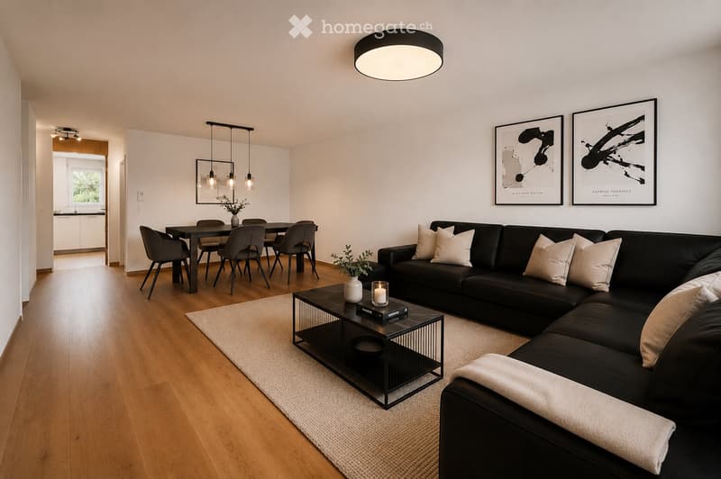 Modern living room with a black sectional sofa, coffee table, dining area with chairs, pendant lights, and artwork on the walls.