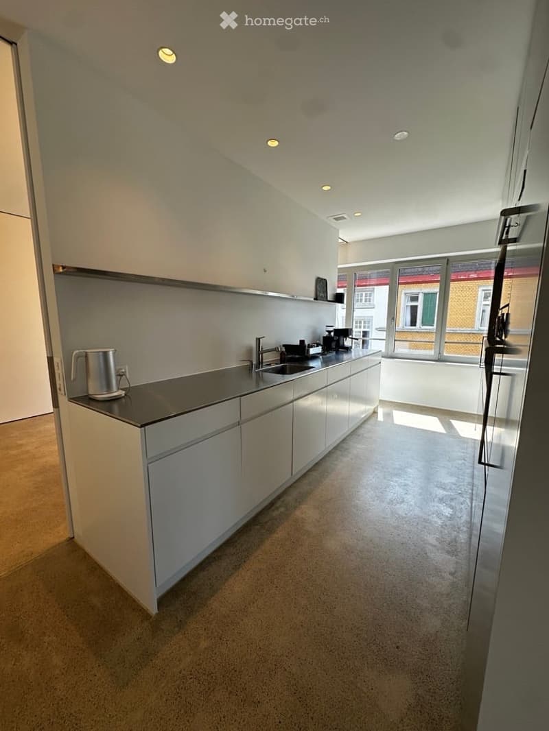 Modern kitchen with white cabinets, stainless steel countertop, and built-in appliances. Features a coffee maker, faucet, and sink.