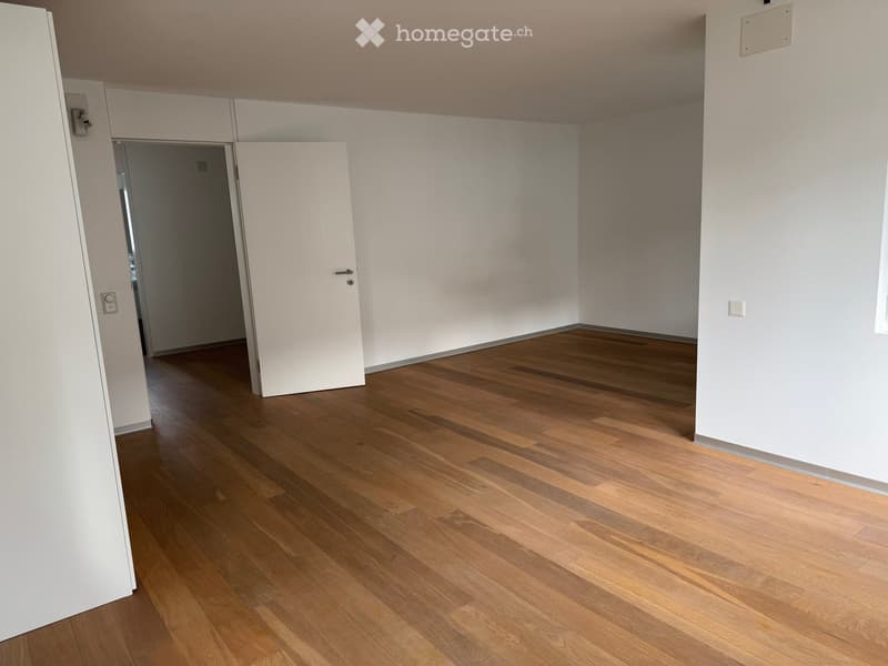 Empty room with wooden flooring and white walls, featuring a closed white door and visible electrical outlets.