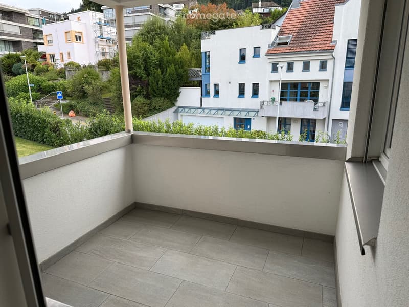Balcony with tiled floor and white walls, overlooking a residential area with modern buildings and greenery.