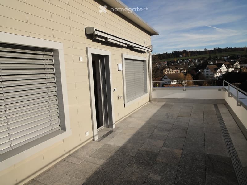 Balcony with tiled floor, white blinds, metal railing, and scenic view of a town and landscape.