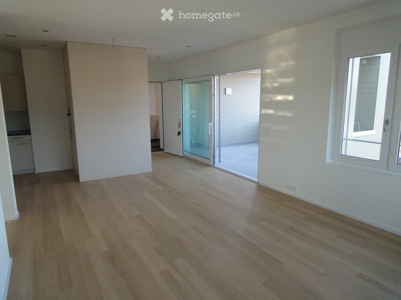Empty room with light wooden flooring, white walls, large window, and sliding glass door leading to a balcony area.