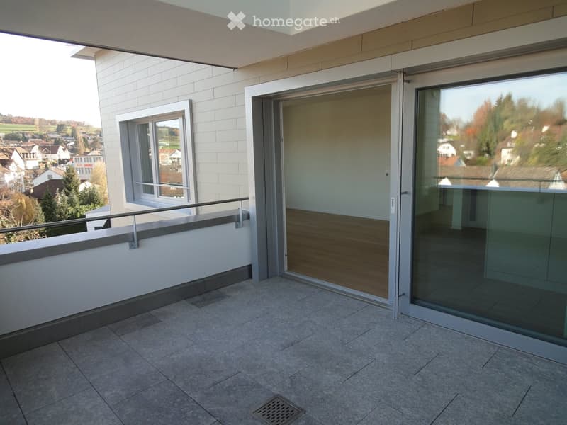 Modern balcony with tiled floor, glass sliding doors, metal railing, and scenic view of the countryside.