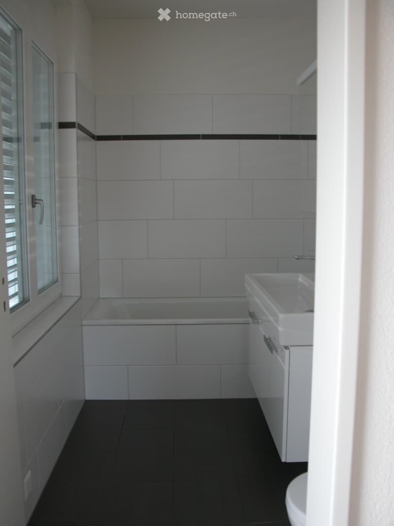 Modern bathroom with white tiles, black accents, bathtub, sink, and toilet.