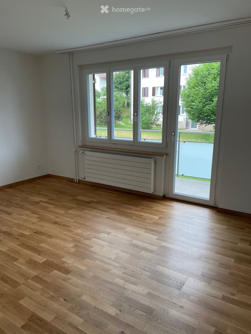 empty room with hardwood floors, sliding doors, windows, radiator