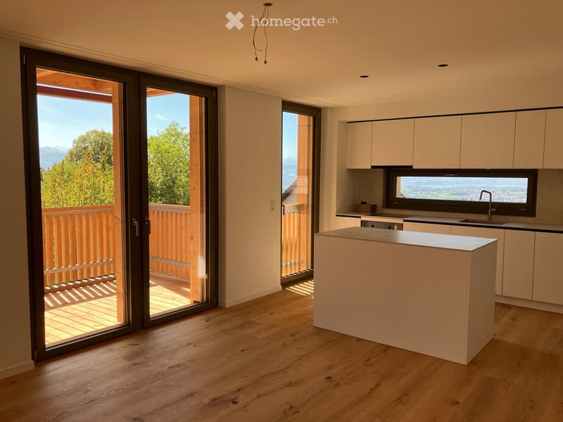 Modern kitchen with light-colored cabinets, a central island, and large sliding glass doors opening to a balcony with a scenic view.