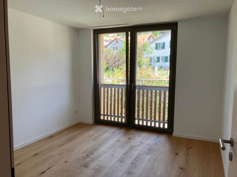 Empty room with light wooden flooring and large sliding glass doors leading to a balcony.