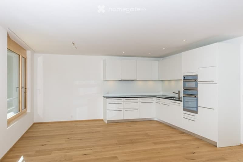 Modern, minimalist kitchen with white cabinetry, wooden flooring, and stainless steel appliances. No furniture or items present.
