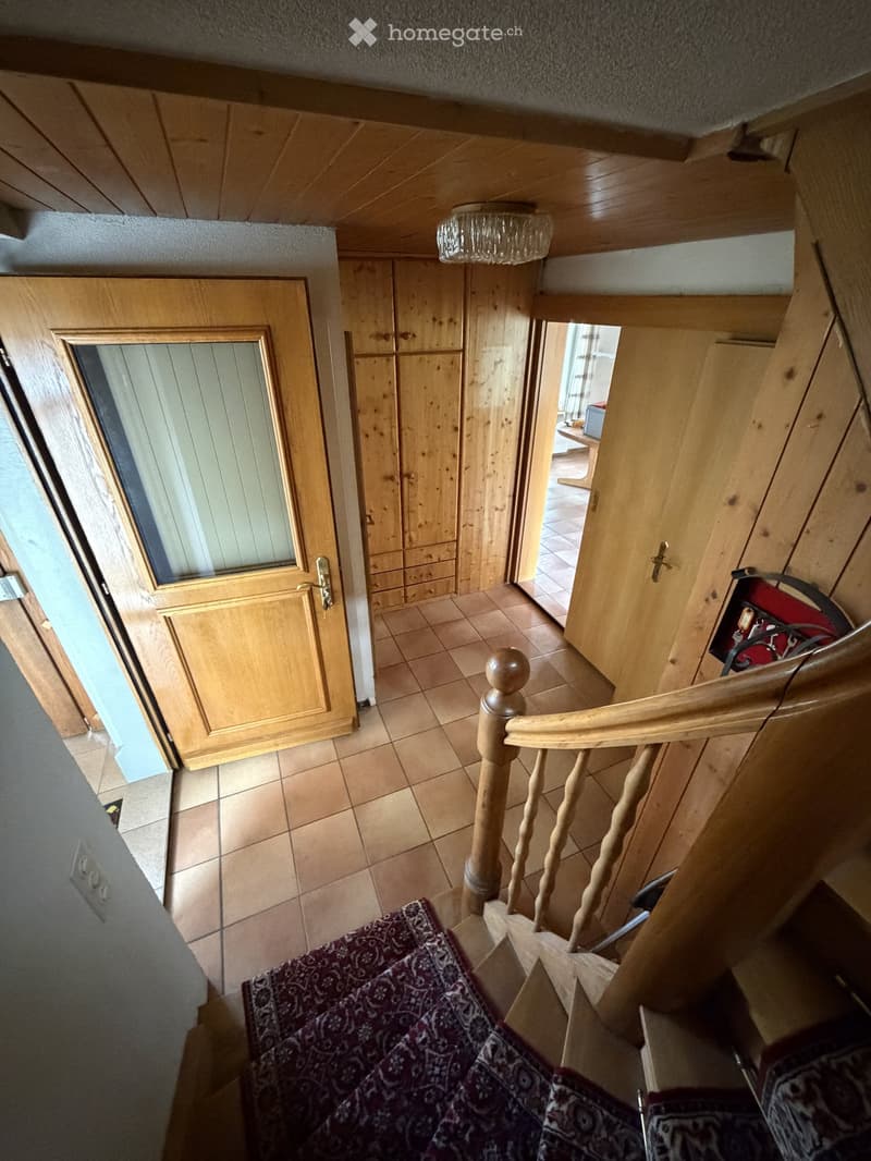 Wooden staircase with a patterned runner, wooden handrail, and a wooden cabinet in the background.