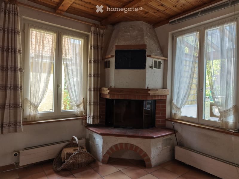 Living room with a stone fireplace, television above it, large windows with curtains, and a wicker basket on the floor.