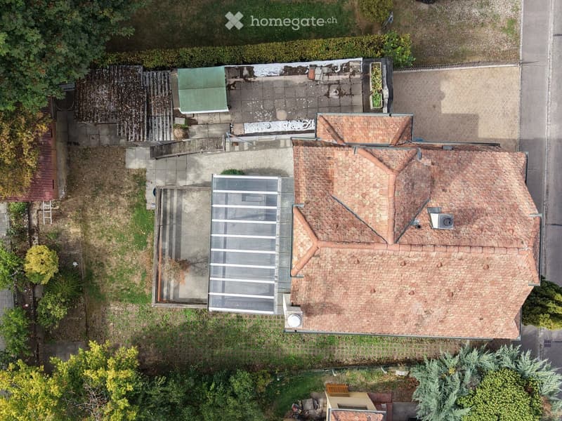 Aerial view of a two-story house with a tiled roof, surrounded by greenery and a small garden area.