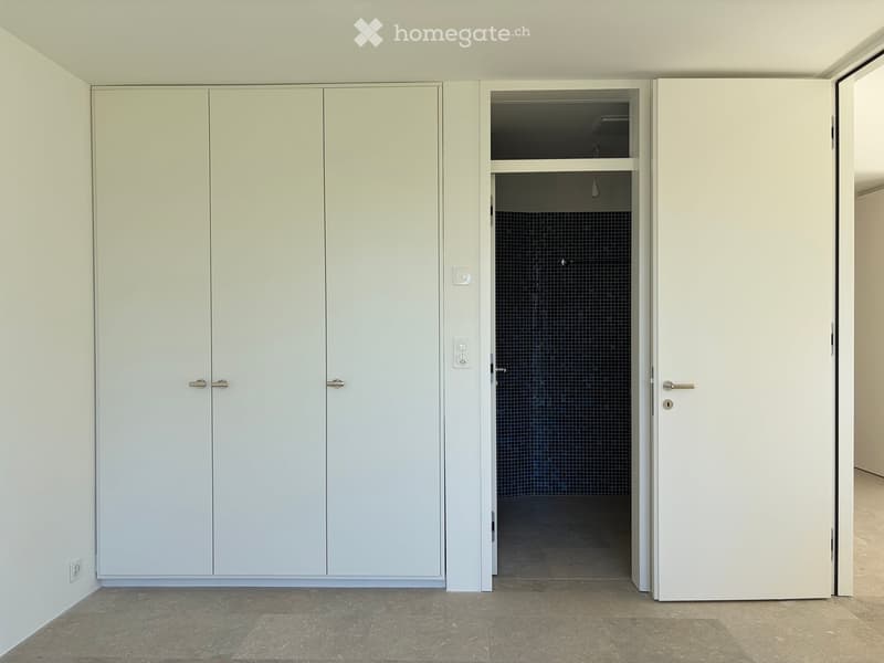 Empty room with white built-in wardrobes and a doorway leading to a tiled bathroom area.