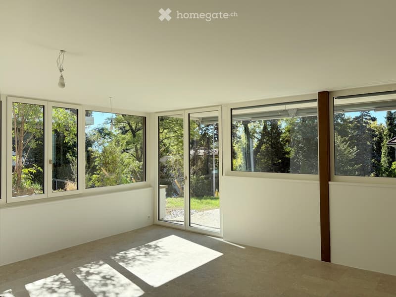 Empty room with large windows and sliding glass doors leading to an outdoor area, featuring light-colored walls and a tiled floor.