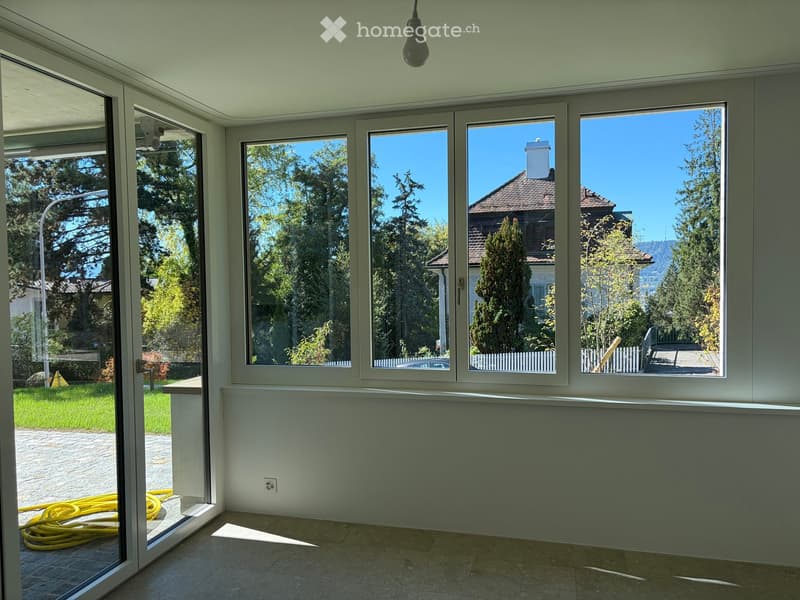 Empty room with large windows and sliding glass doors, tiled floor, and visible outdoor area with trees and a house.