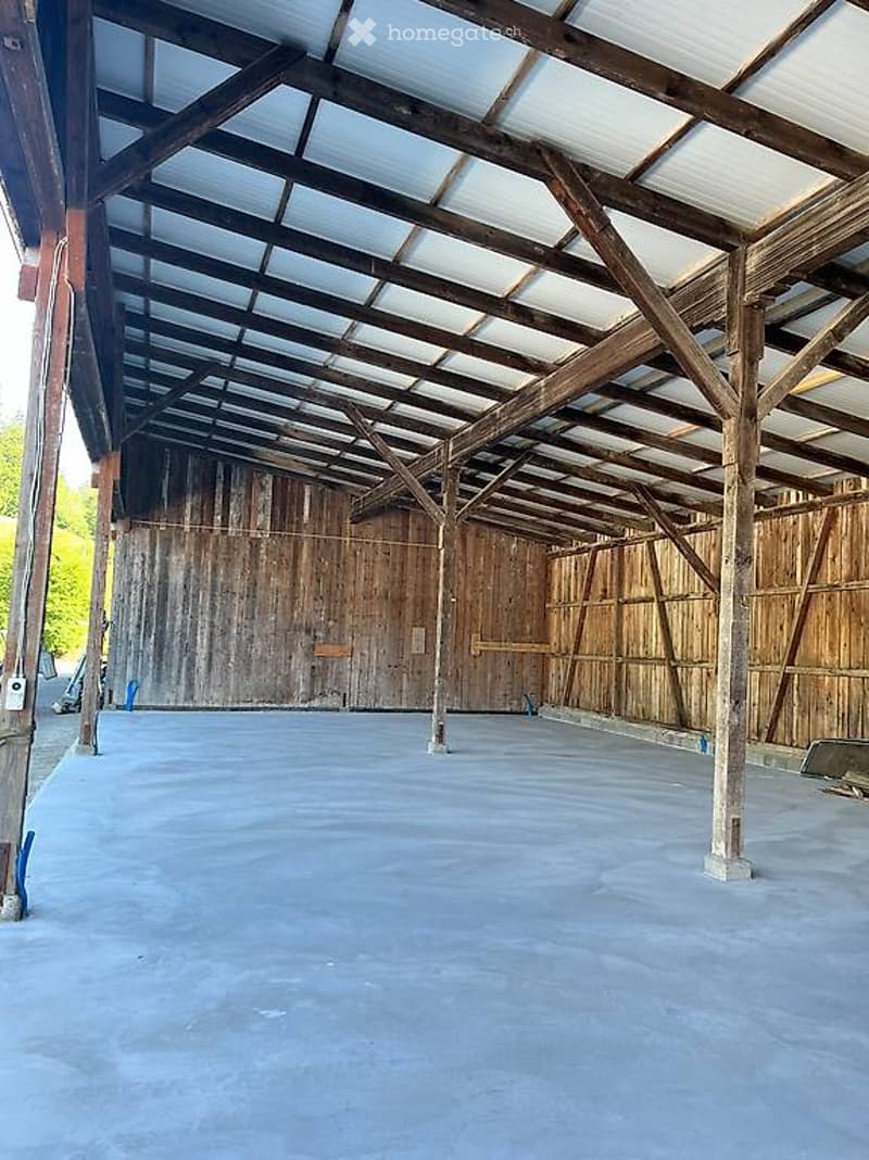 Empty wooden barn with a concrete floor, exposed wooden beams, and a metal roof. No furniture or equipment present.