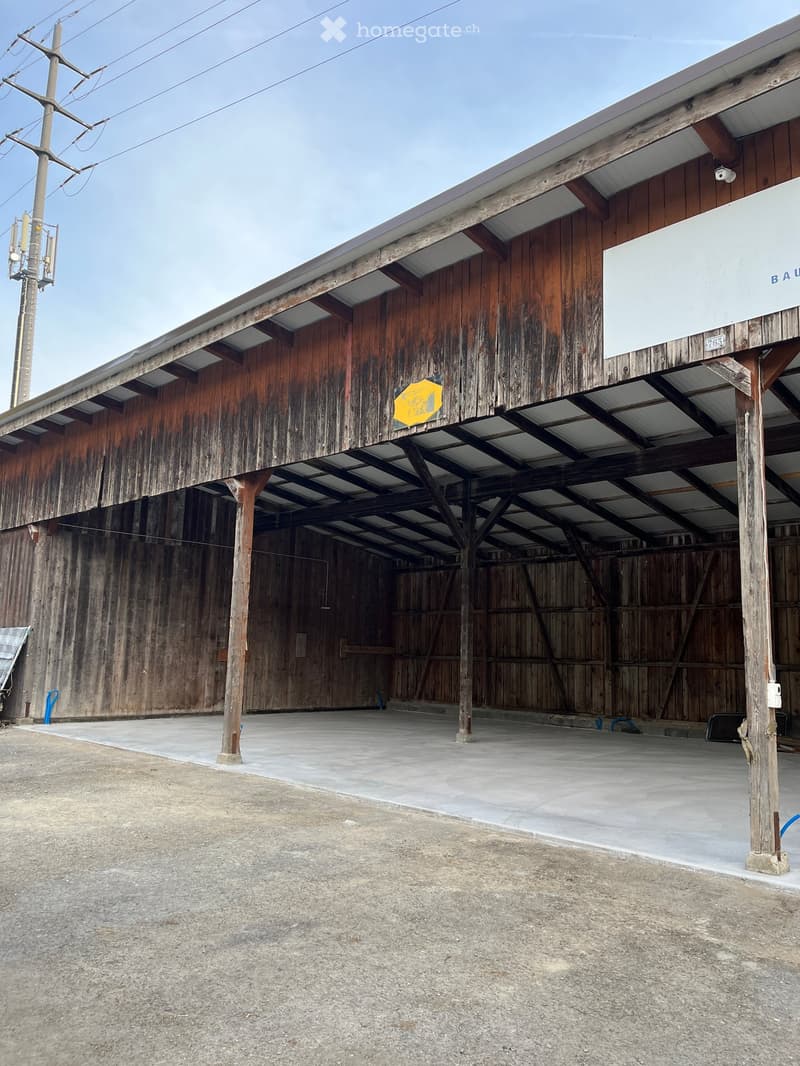 Large wooden barn with a covered open area, concrete floor, and metal roof supported by wooden beams.