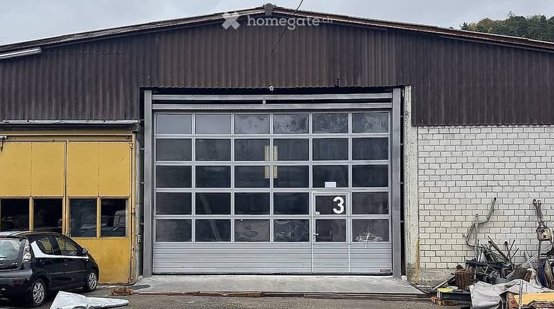 Industrial-style building with a large garage door marked with the number 3, adjacent to a smaller yellow door, and a parked car nearby.