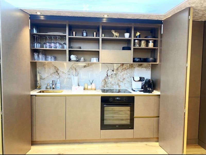 Modern kitchen with light wood cabinets, marble backsplash, stainless steel appliances, and open shelving displaying glassware and dishes.