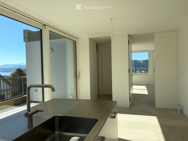 Modern kitchen with a sleek stainless steel sink and faucet, large windows offering scenic views, and open floor plan connecting to a hallway.