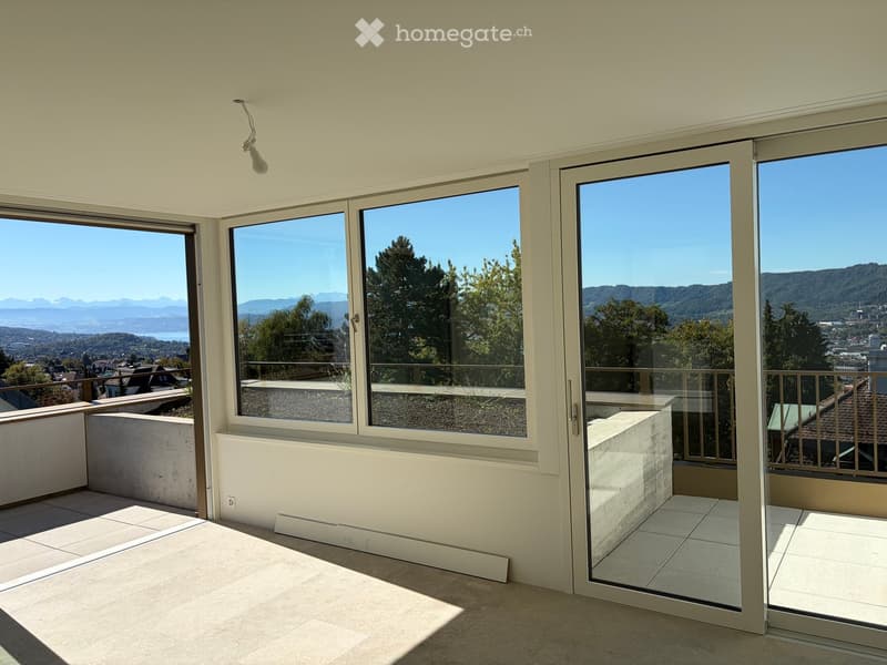 Empty room with large windows and sliding glass doors offering a scenic mountain view. The room has tiled flooring and white walls.