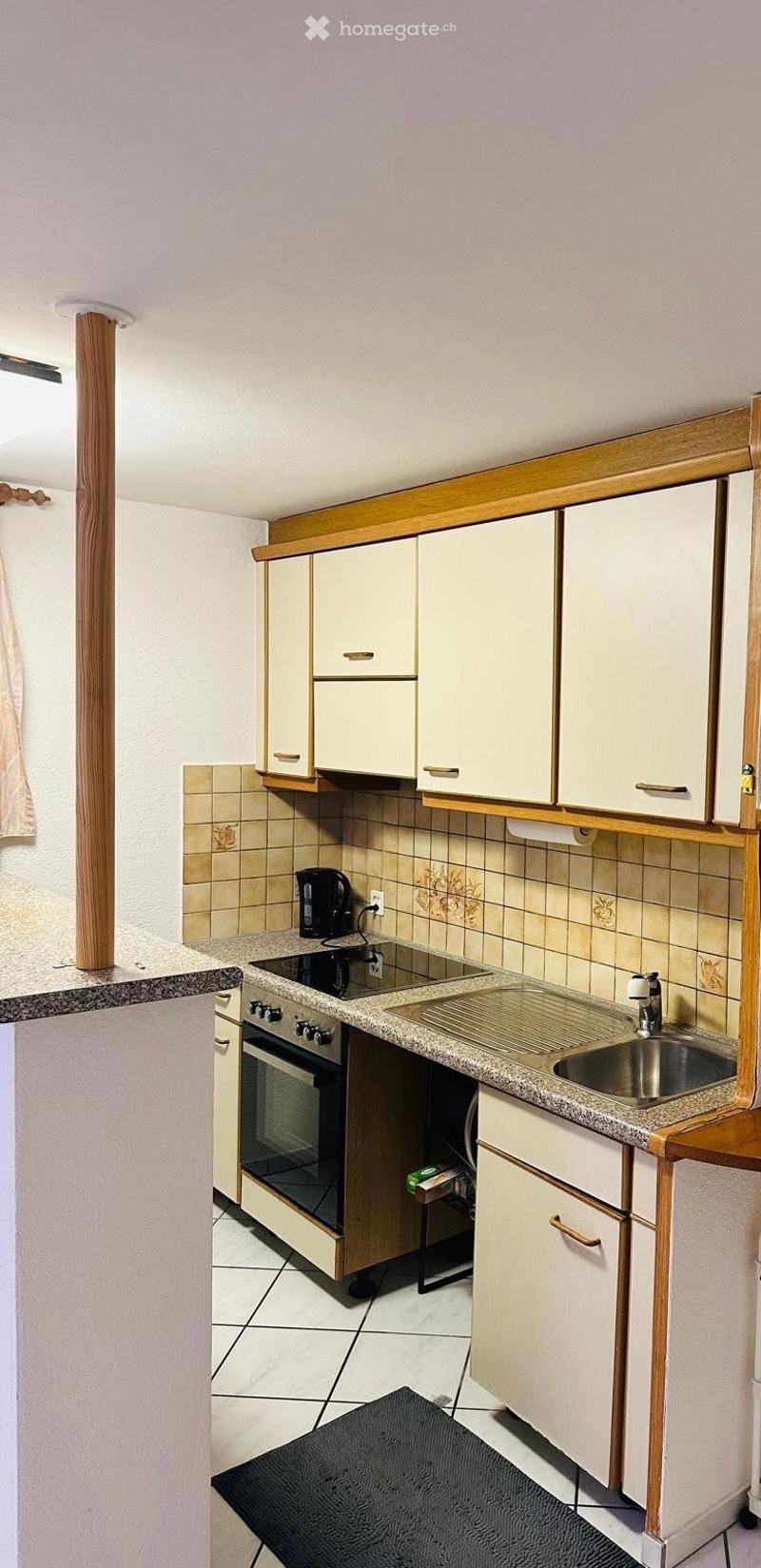 A compact kitchen with white cabinets, a granite countertop, a sink, an oven, and a coffee maker. The walls are tiled, and the floor is tiled as well.