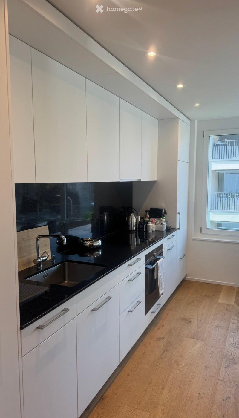 Modern kitchen with white cabinets, black countertops, stainless steel sink, and various appliances.