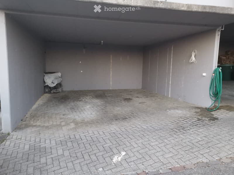 Empty outdoor space with brick pavement, grey walls, and a covered area. No furniture or equipment present.