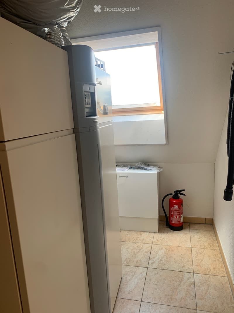 Empty utility room with tiled floor, white walls, a window, a water softener, a small cabinet, and a red fire extinguisher.