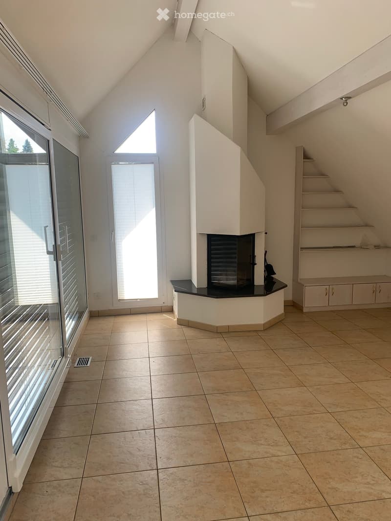 Empty room with tiled floor, white walls, fireplace, large windows, and a staircase leading upwards.