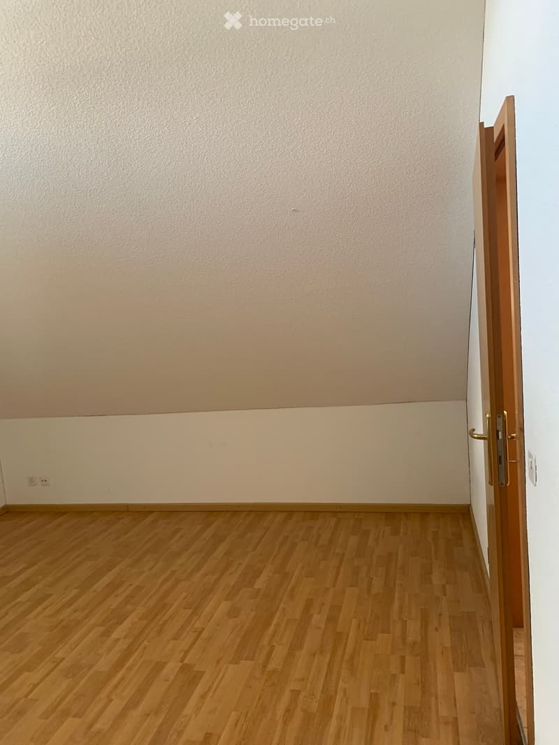 Empty room with wooden flooring and white walls, featuring a partially open wooden door on the right side.