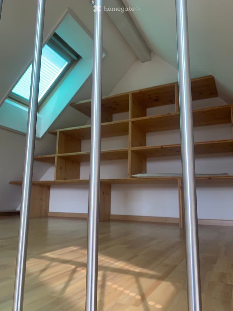 Empty attic room with wooden flooring, built-in wooden shelving units, and skylight windows allowing natural light to enter.