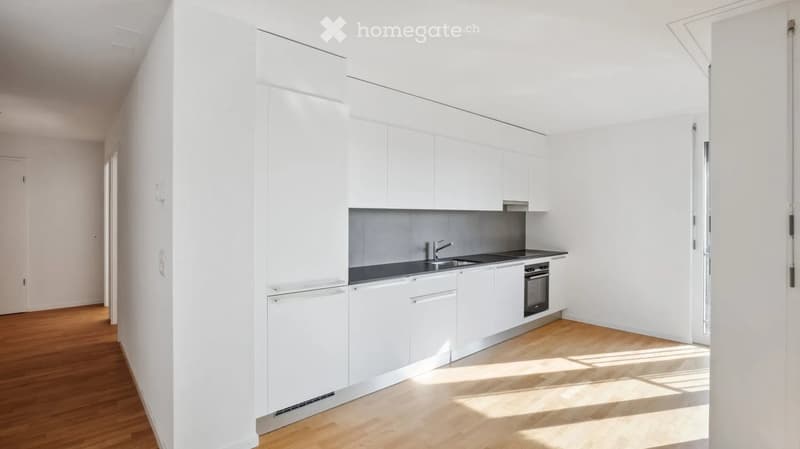 Modern, minimalist kitchen with white cabinets, a dark countertop, and a wooden floor. Features a sink, faucet, and built-in oven.
