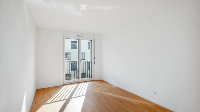 Empty room with white walls, wooden floor, and large glass sliding doors leading to a balcony.