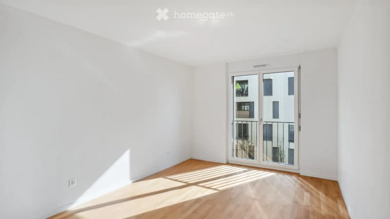 Empty room with white walls and wooden flooring, featuring a large sliding glass door leading to a balcony.