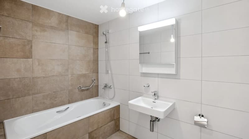 Modern bathroom with a bathtub, sink, mirror, and shower area. Features beige tiles and white fixtures.
