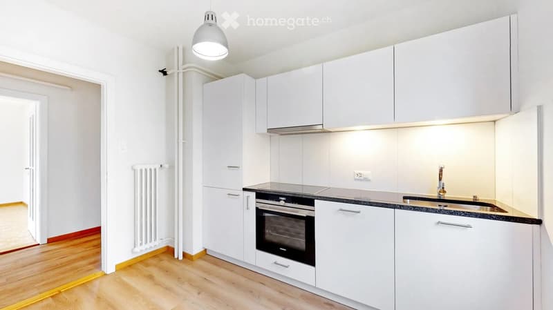 Modern kitchen with white cabinets, black countertop, built-in oven, sink, and pendant light fixture.