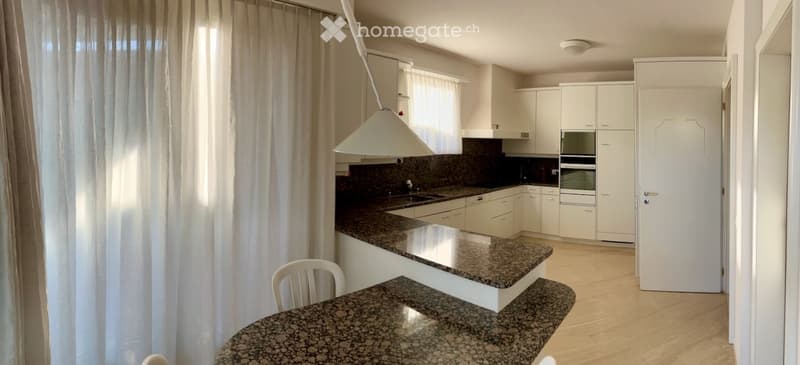 Modern kitchen with white cabinets, granite countertops, built-in oven, and a pendant light hanging over the island.