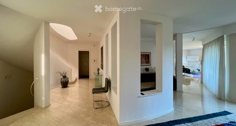 Modern hallway with white walls, beige tiled floor, and a glass table with a vase. A green chair is placed near the wall, and a staircase leads upwards.