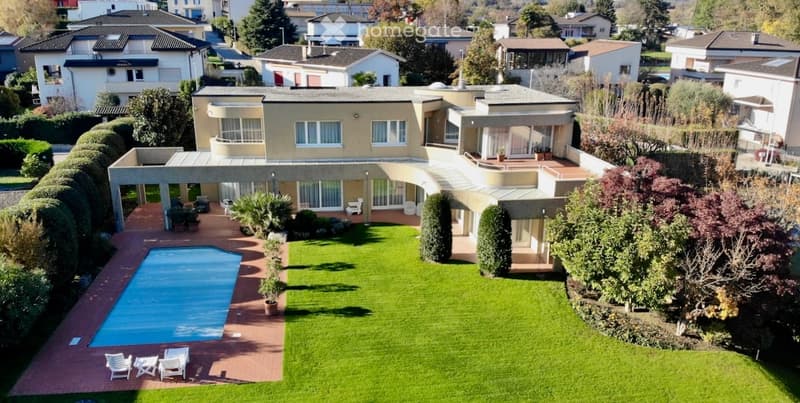 Aerial view of a large, modern house with a well-maintained garden, a swimming pool, and outdoor seating areas.