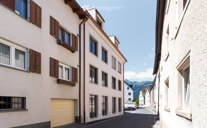 A row of residential buildings with white facades, wooden shutters, and a visible garage entrance.