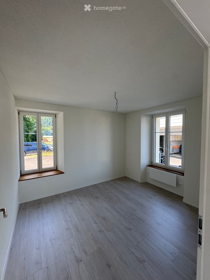 Empty room with light grey walls, wooden flooring, and large windows with wooden sills. No furniture or equipment present.