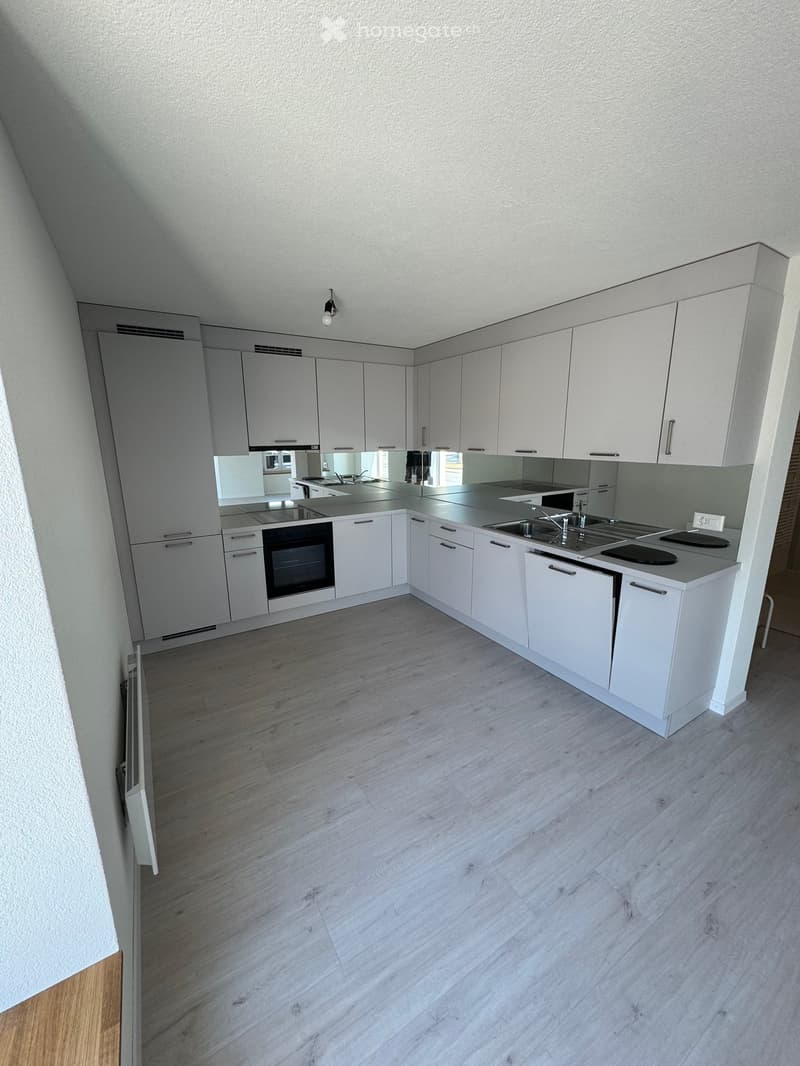Modern kitchen with white cabinets, a central island, and a sink, featuring a sleek design and light wood flooring.