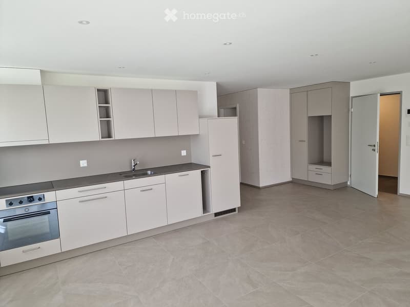 Modern kitchen with light grey cabinets, stainless steel oven, sink, and faucet. Open space with tiled floor and recessed lighting.