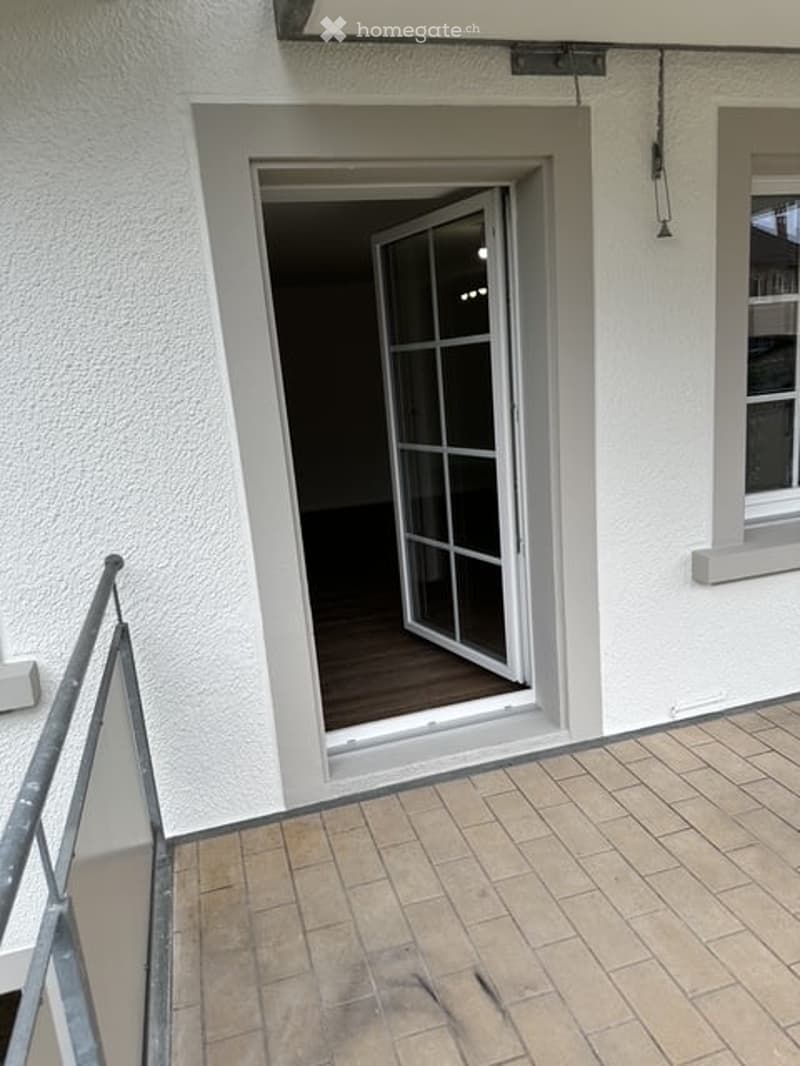 Balcony with tiled floor, metal railing, and an open sliding door leading to an interior space.